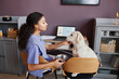 © Seventyfour - Side view portrait of young black woman petting cute dog sitting on chairs together and working