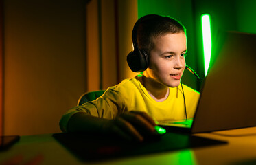 Young boy gamer with headphone playing video game on laptop at home.