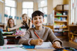 © Maskot - Portrait of happy male pupil sitting at desk in classroom