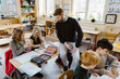 © Maskot - Male teacher sitting on desk and watching students studying in classroom