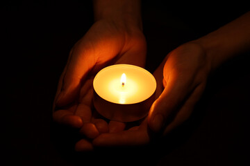 Woman holding burning candle in hands on black background, closeup