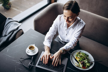 Canvas Print - Woman working on laptop and eating salad with coffee, top view