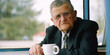 © Marcela Ruty Romero - Grandpa in a suit with a cup of coffee in his hands sitting at a table. Generative AI