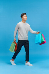 Wall Mural - Young asian man shopaholic smiling while holding shopping bags isolated on blue