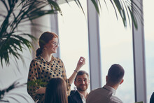 A Group Of Young Business Professionals In A Modern Office Attentively Listens To Colleague Presentation, Showcasing A Dynamic And Collaborative Atmosphere As They Exchange Ideas And Strive For