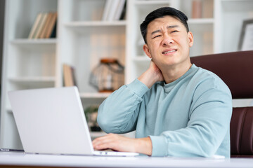 Millennial tired stressed man having a neck pain. Male touching massaging neck sitting at the desk working or studying indoors, suffering from discomfort long hours of sedentary overworking concept