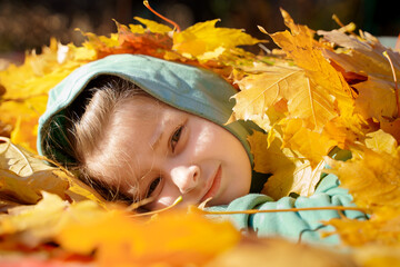Girl kid girl is lying on ground on autumn leaves. Bright yellow orange maple foliage. Child walking, having fun, playing in fall backyard. Outdoor funny happy season family activity in autumn park