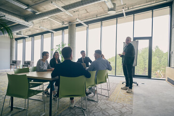 In a modern office setting, a group of business professionals attentively listens to a captivating presentation delivered by their young colleagues, showcasing their teamwork, engagement, and