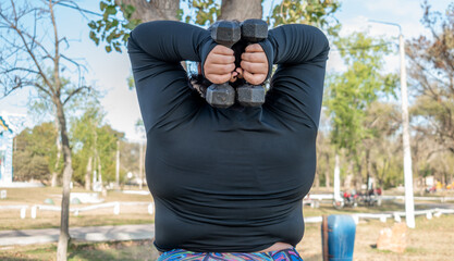 Wall Mural - Young fat woman exercising with dumbbells in the park by the lake. Healthy lifestyle