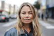 © ADDICTIVE STOCK - Generative AI illustration of positive middle age female with long blond hair smiling and looking at camera while standing on street in city