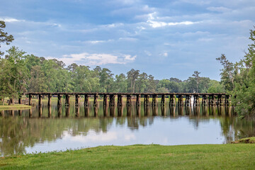 A railroad track bridge over a public lake called Cherokee Lake, in Thomasville Georgia on a Sunny day with a tranquil and peaceful scene