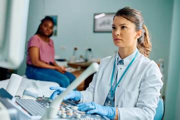 Wall Mural - Female doctor using ultrasound during appointment with African American woman at clinic.