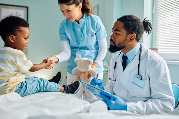 Wall Mural - Small black kid shaking hands with nurse during medical checkup at doctor's office.