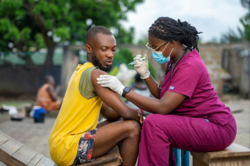 image of african guy receiving medical treatment from home- black nurse in facemask injecting a youn