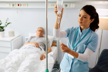 Nurse practitioner checking IV drip of senior patient at hospital ward.