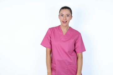 young caucasian doctor woman wearing pink uniform over white background  having stunned and shocked look, with mouth open and jaw dropped exclaiming: Wow, I can't believe this. Surprise and shock