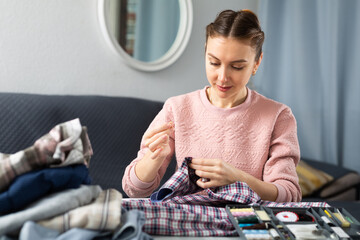 Wall Mural - Portrait of young woman housewife stitching button on shirt