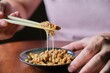 Unrecognizable man eating natto fermented soy beans with chopsticks.