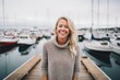 © Leon Waltz - Medium shot portrait photography of a grinning woman in her 30s that is wearing a cozy sweater against a bustling marina with yachts and sailboats background .  Generative AI