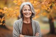 © Leon Waltz - Portrait of a smiling senior woman standing with arms crossed in autumn park