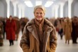 © Leon Waltz - Medium shot portrait photography of a grinning woman in her 60s that is wearing a warm parka against an elegant fashion show runway with models background .  Generative AI