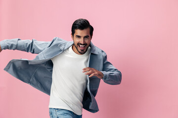 Wall Mural - Stylish brunette man with beard happiness open mouth jumping and running spreading his arms on a pink background in a white T-shirt and jeans smile and joyful emotion on his face, copy space