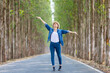 © Akarawut - Asian tourist woman is jumping and dancing while having vacation at the national park while walking on the road with column of tree for travel and adventure