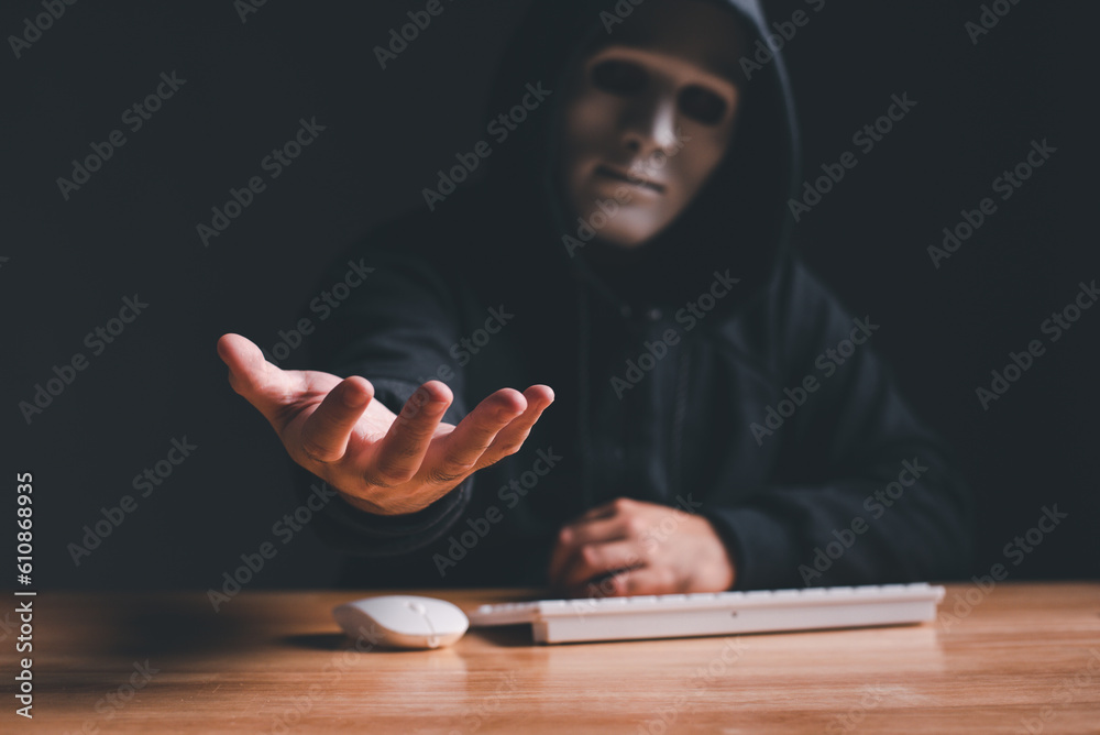 Black hood hacker force demands ransom by holding out his hand on table ...