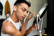 Biracial transgender man looking in mirror and putting on make-up, brushing eyebrows