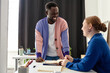 © Seventyfour - Waist up portrait of cheerful black man talking to colleague in office wearing colorful outfits