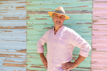 Portrait of caucasian senior man wearing hat with hands on hip standing against wooden wall