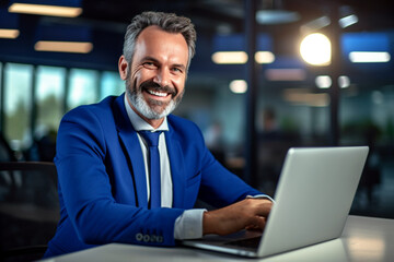 Wall Mural - Happy smiling middle aged professional business company executive manager in blue suit sitting at desk in office working on laptop computer laughing at workplace. made with ai