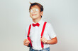 A boy with glasses with a satisfied smile holds on to his red suspenders.