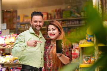 Indian couple showing smartphone screen at grocery shop.