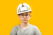 Portrait of teenage boy wearing glasses and protective white helmet isolated on yellow background. Child is like builder or an engineer.