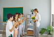 © Studio Romantic - Children students giving flowers to their teacher clapping hands congratulating on holiday at elementary school. They smiling and looking at her in classroom. Good attitude, care and respect concept.