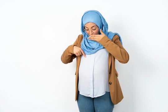 Shocked Young beautiful pregnant muslim woman wearing hijab over white background look surprisedly down, indicates at blank  with fore finger, Scared model