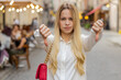 © Andrii Iemelianenko - Dislike. Upset blonde young woman showing thumbs down sign gesture, expressing discontent, disapproval, dissatisfied bad work, mistake. Displeased teenager girl walking in urban city street outdoors