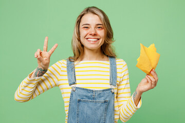 Wall Mural - Sick unhealthy ill allergic woman has red watery eyes runny stuffy sore nose suffer from allergy trigger symptoms hay fever hold napkin show v-sign isolated on plain green background studio portrait.