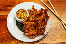 A Plate Of Crispy Fried Pigs Ear With A Spicy Sauce On A White Plate Against A Wooden Surface, Chopsticks Nearby