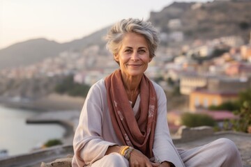 Wall Mural - Close-up portrait photography of a satisfied mature woman meditating against a scenic cliffside village background. With generative AI technology