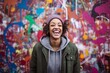 © Markus Schröder - Lifestyle portrait photography of a grinning girl in her 30s wearing a stylish hoodie against a colorful graffiti wall background. With generative AI technology