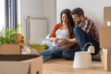 A young happy married couple expecting a baby sitting on the floor of their new home after moving in. Unpacking after relocation. New homeowners. New beginnings