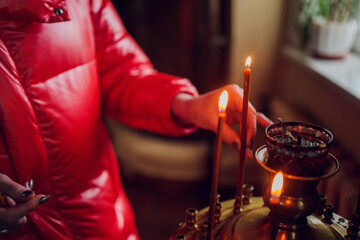 Wall Mural - Woman's hand in a red jacket puts a church candle.