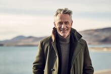 Lifestyle Portrait Photography Of A Grinning Mature Man Wearing A Cozy Winter Coat Against A Scenic Lagoon Background. With Generative AI Technology