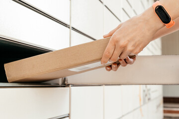 Wall Mural - A woman with a box in his hands near the self-service mail terminal. Parcel delivery machine. Person holding a cardboard box. Mail delivery and post service, online shopping, e commerce concept