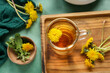 Board with glass cup of healthy dandelion tea on green background