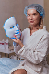 Wall Mural - LED light anti-aging mask for facial skin care in a spa slow motion. A woman lies on a couch in a special mask. Modern technologies of beauty and health.