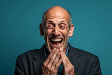 Poster - Headshot portrait photography of a grinning mature man placing the hand over the mouth in a laughter gesture against a sea-green background. With generative AI technology