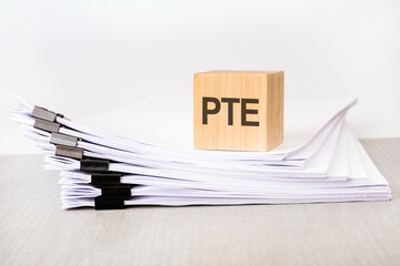 Poster - a wooden cube with a text PTE on a stack of documents. grey table, white background